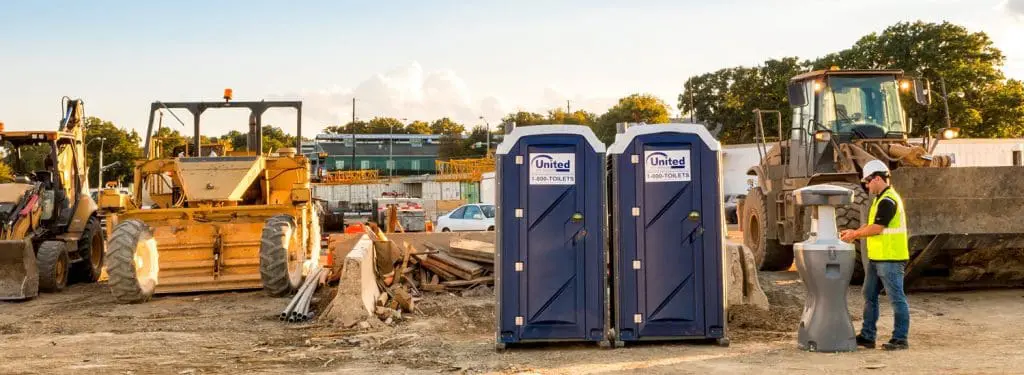 a construction site with heavy machinery and two porta potties and a hand washing station