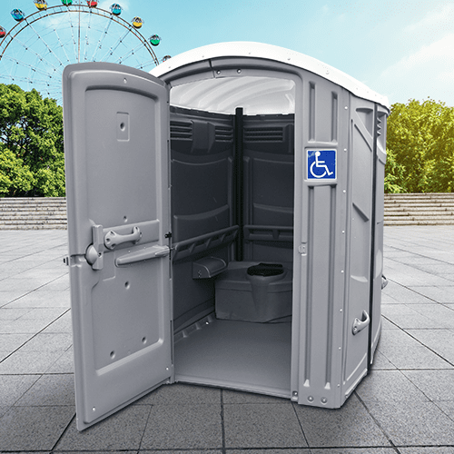A wheelchair-accessible portable restroom with an open door revealing an interior with handrails, located outdoors with a ferris wheel in the background