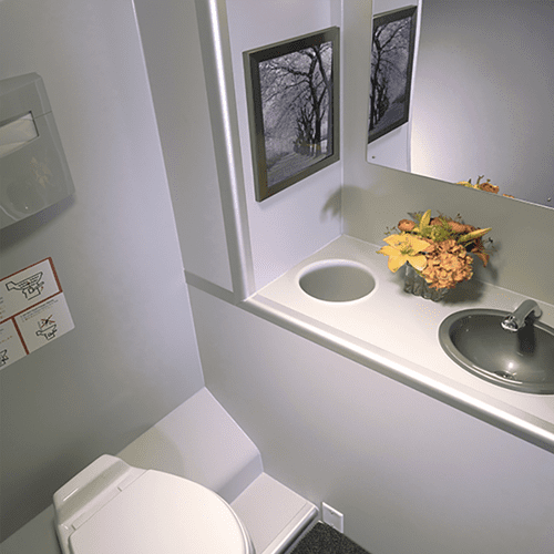 Trailer restroom with a white toilet, small built-in sink, vanity mirror, and decorations