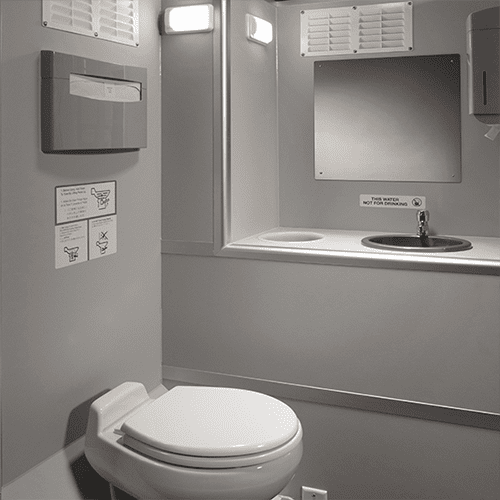 Interior of a restroom trailer with toilet on the left and a sink with a mirror above on the right
