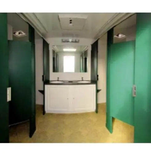 Interior of a trailer restroom with green stall doors, white sinks, and mirrors against a cream wall