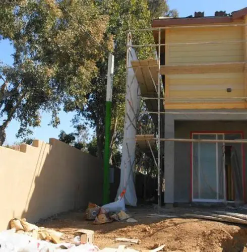 A house under construction with unfinished wooden facades, a scaffolding setup on the side, and construction debris scattered around the site