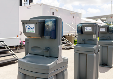3 portable hand washing stations with two bathroom trailers behind them